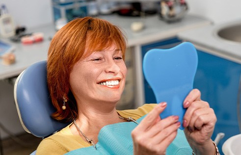 A woman smiling in the mirror at her new dentures