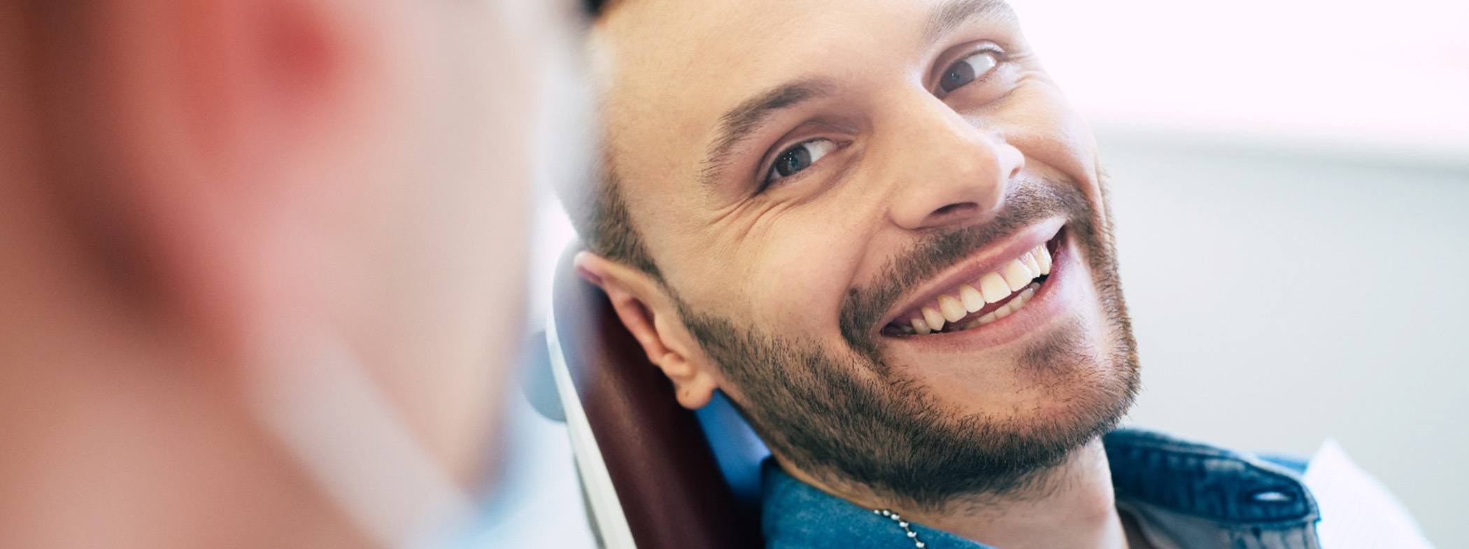 Man in denim shirt in dental chair smiling at dentist