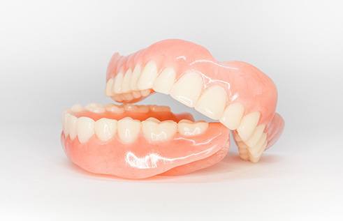 Upper arch of dentures resting on lower arch of dentures on white surface