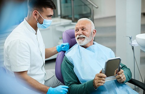 Senior patient looking at dentist while holding small mirror