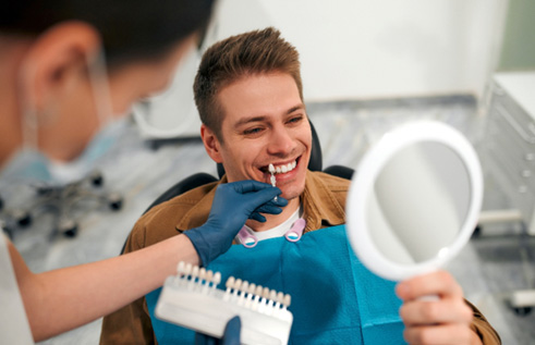 a smiling man looking in a handheld mirror at the dentist’s office